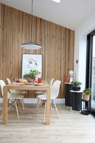 Dining area of open-plan space with oak table, white chairs, laminate flooring and slatted panelled wall