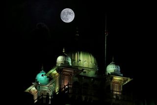 Super blue moon shines above a large building with several domes on the roof.