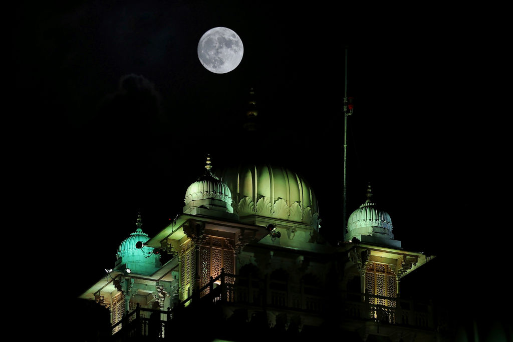 Uma lua azul gigante brilha sobre um grande edifício com várias cúpulas no telhado.