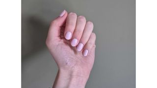 A close-up of Digital Beauty Writer, Naomi Jamieson's short pastel pink nails/ pictured in front of a dark green wall