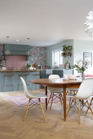 Green shaker kitchen diner with house plants, rug, and pink tiled splash back