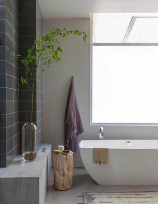 A bathtub with a hanging towel. Near the ledge is a stem plant in a fine glass vase