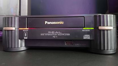 Close up of Panasonic 3DO console on black desk with red ready and green access lights illuminated.