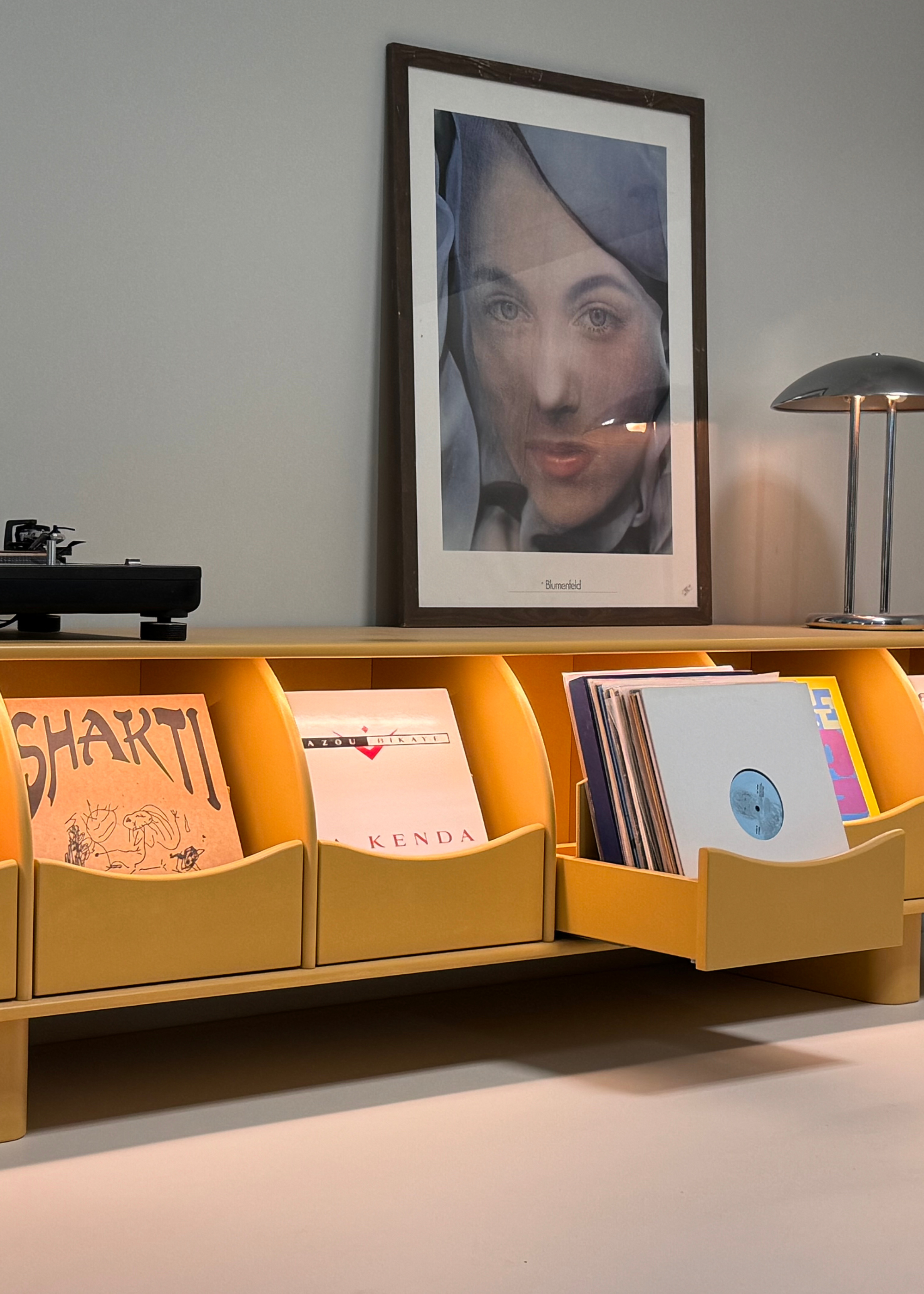 A yellow record bar with soft lighting in a living room with a chrome lamp, a turntable and framed art
