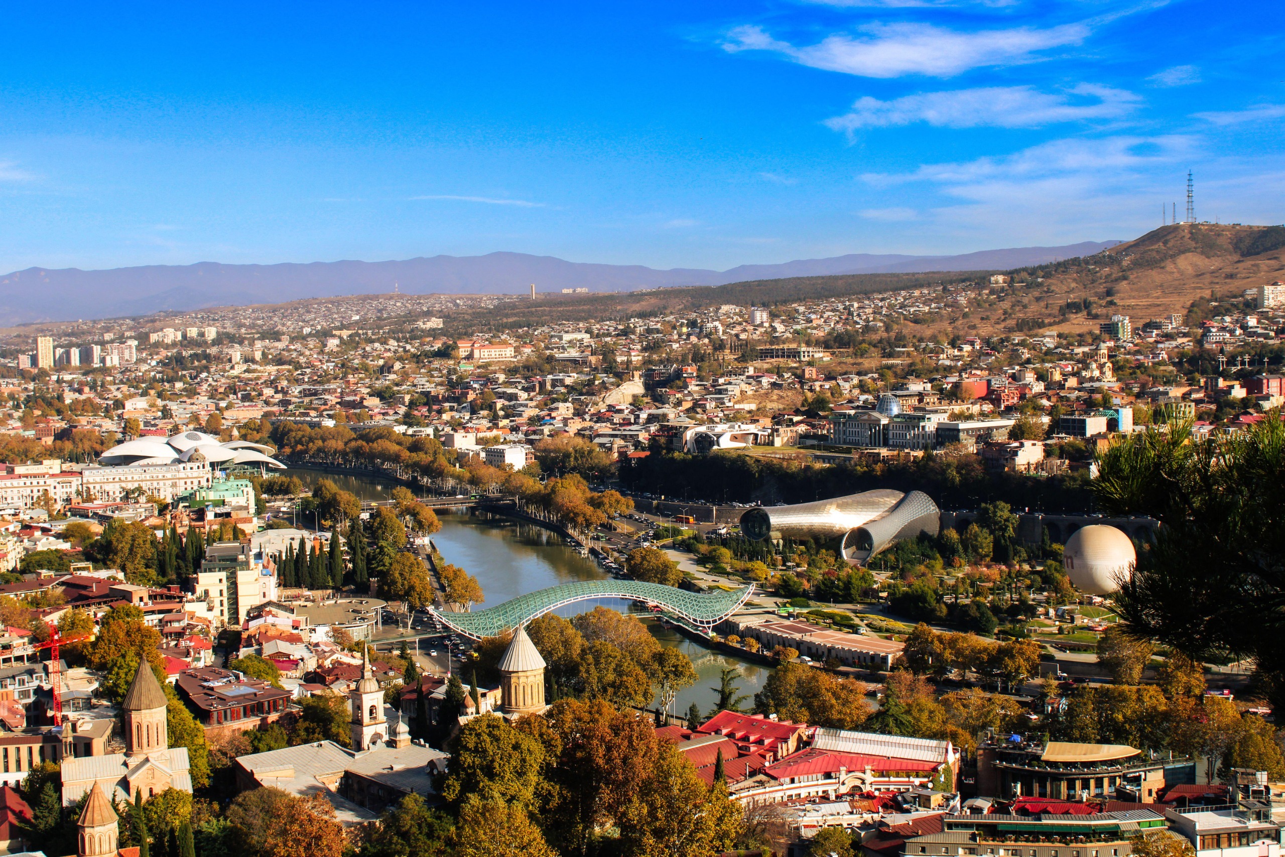 An aerial view of the city of Tbilisi in Georgia, showing mountains, and a mix of classic and modern buildings