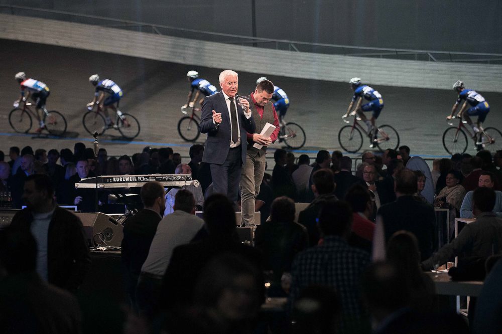 Riders circle the track while Patrick Lefevere addresses the crowd.