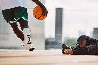 Photographer lying on the ground of a basketball court with a Canon EOS R1, photographing the action