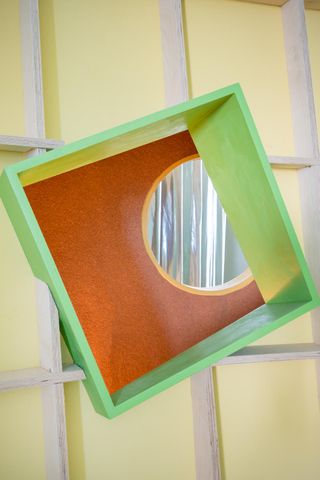 View through a green window frame to the interior of a playhouse made from plywood and featuring geometric shapes.