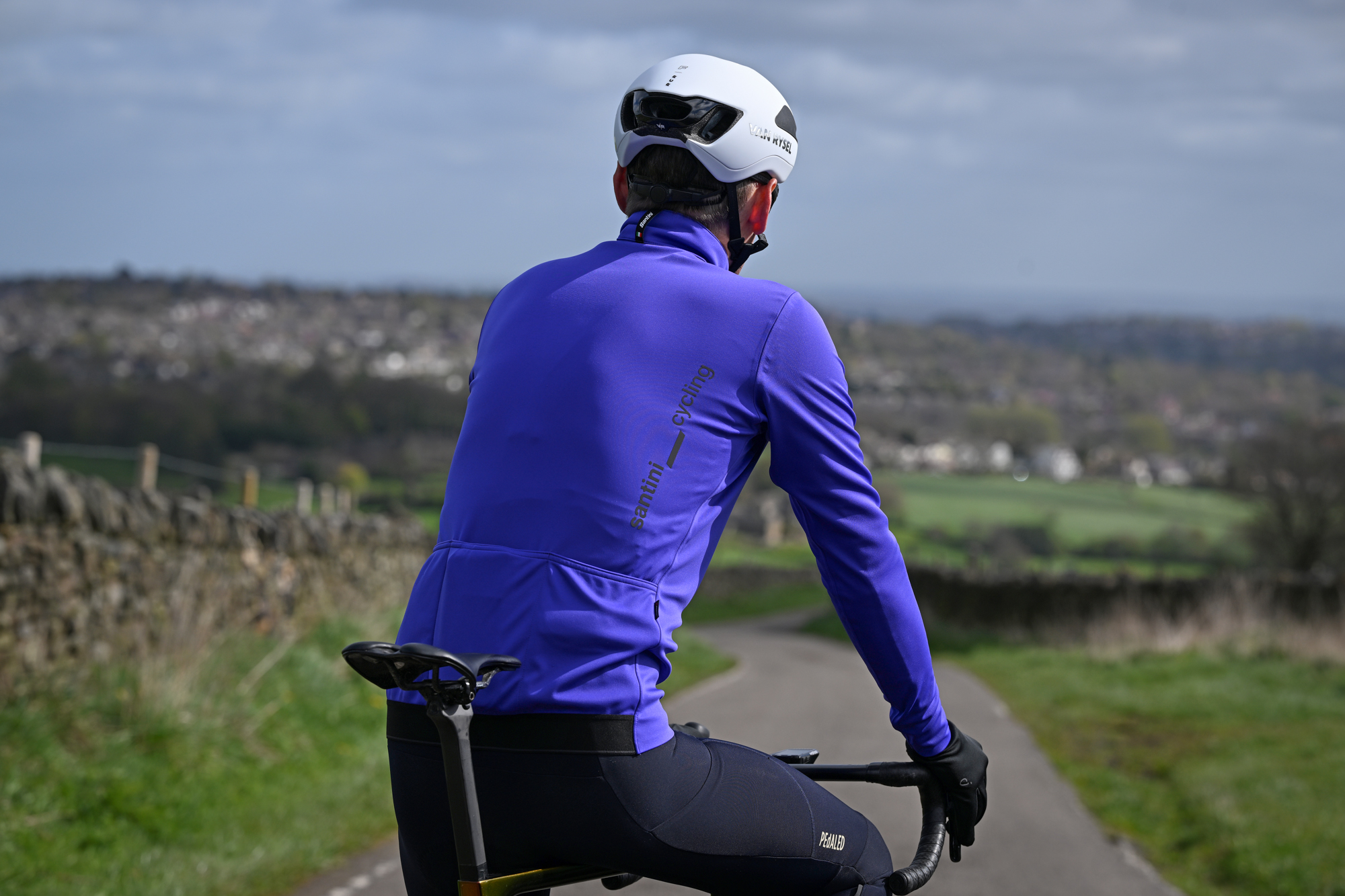 rear view of a man in a purple jacket,and white helmet sitting on his bike on a country lane