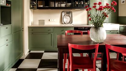 A sage green kitchen with red chairs and flowers