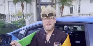 Jake Paul looking like a villain, smoking a cigar while leaning against his car.