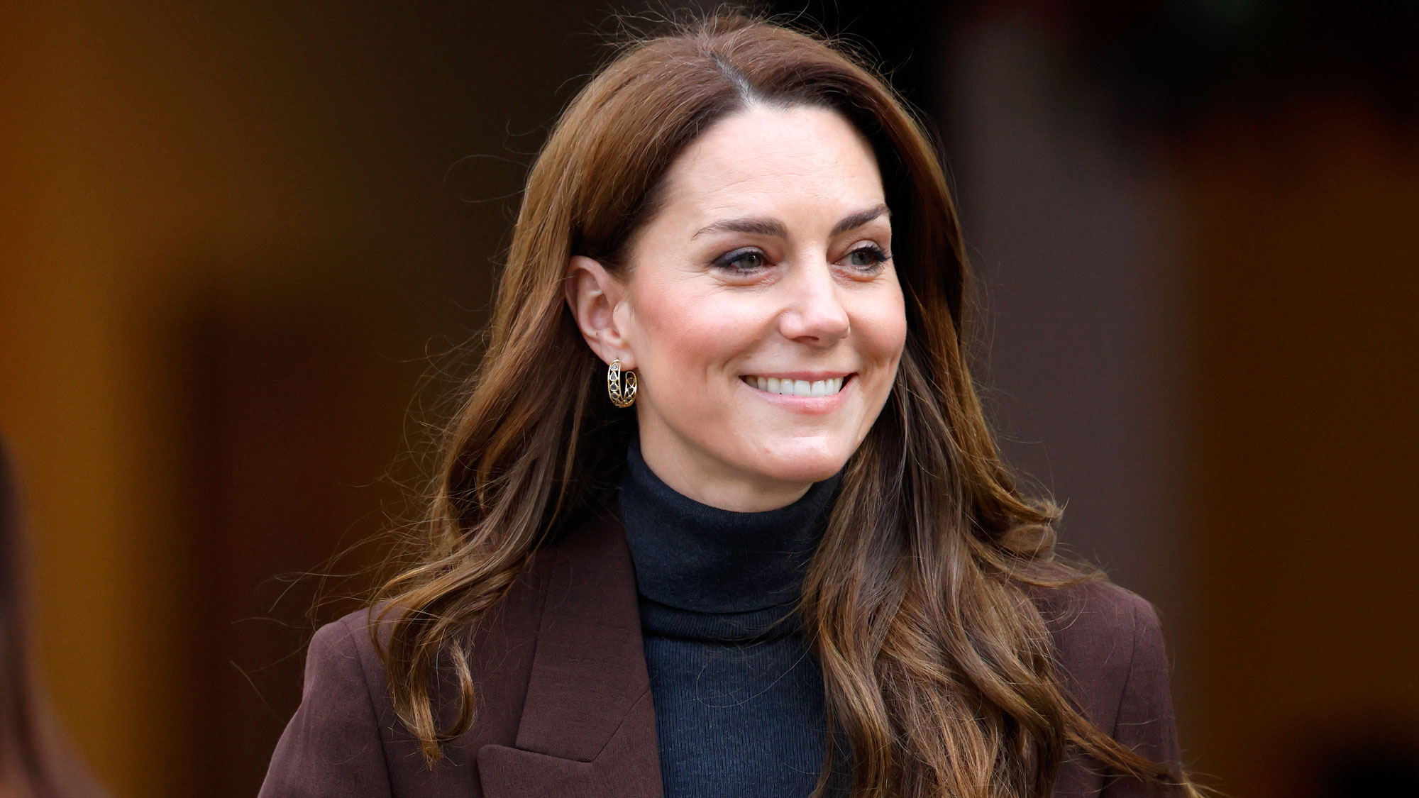 Kate Middleton wears a burgundy coat and a navy turtleneck sweater