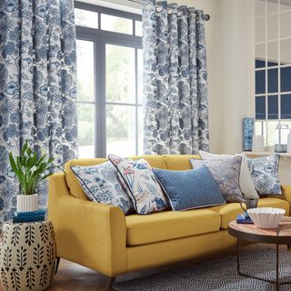 accent colour ideas, living room with blue patterned curtains and cushions, yellow sofa, plant, coffee table, graphic rug