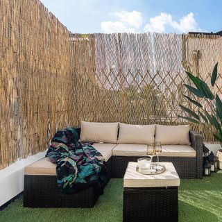Roof terrace with wicker corner sofa, fake grass and patterned throw