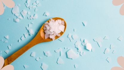 A shot of salts in a wooden spoon on a blue backdrop, to illustrate the Epsom salt benefits can have on your skin, body, and mind