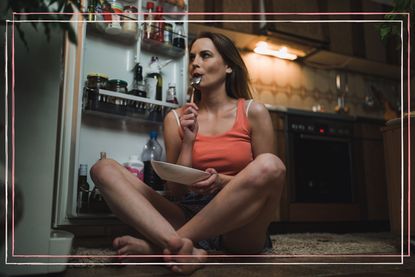 A woman in pyjamas sat on the floor next to an open fridge