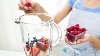 A woman adding raspberries to a vblender which already has soft fruits in it