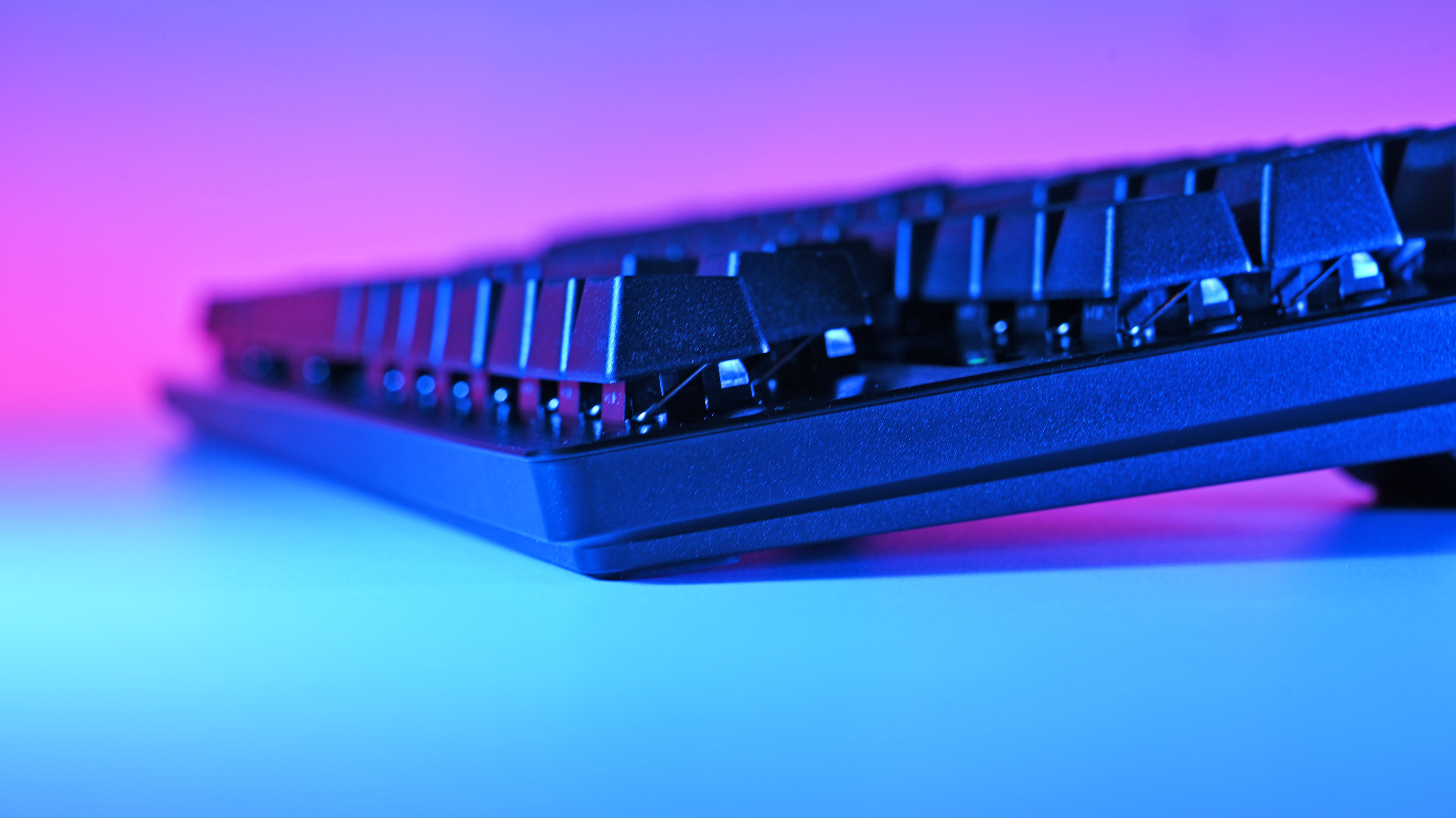 Close-up of Razer Huntsman V3 Pro TKL 8KHz keyboard with raised keys, illuminated by blue and pink lighting from below, creating a vibrant, futuristic atmosphere.