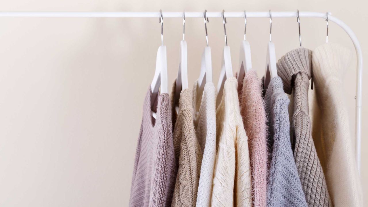 jumpers hanging on a white rack, against a beige wall