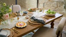 Spring tablescape accented with brass tableware, woven chargers, cream dinner plates, and navy blue table linens.