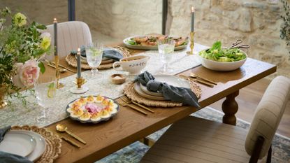 Spring tablescape accented with brass tableware, woven chargers, cream dinner plates, and navy blue table linens.