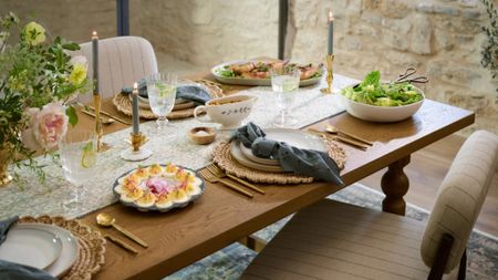 Spring tablescape accented with brass tableware, woven chargers, cream dinner plates, and navy blue table linens.