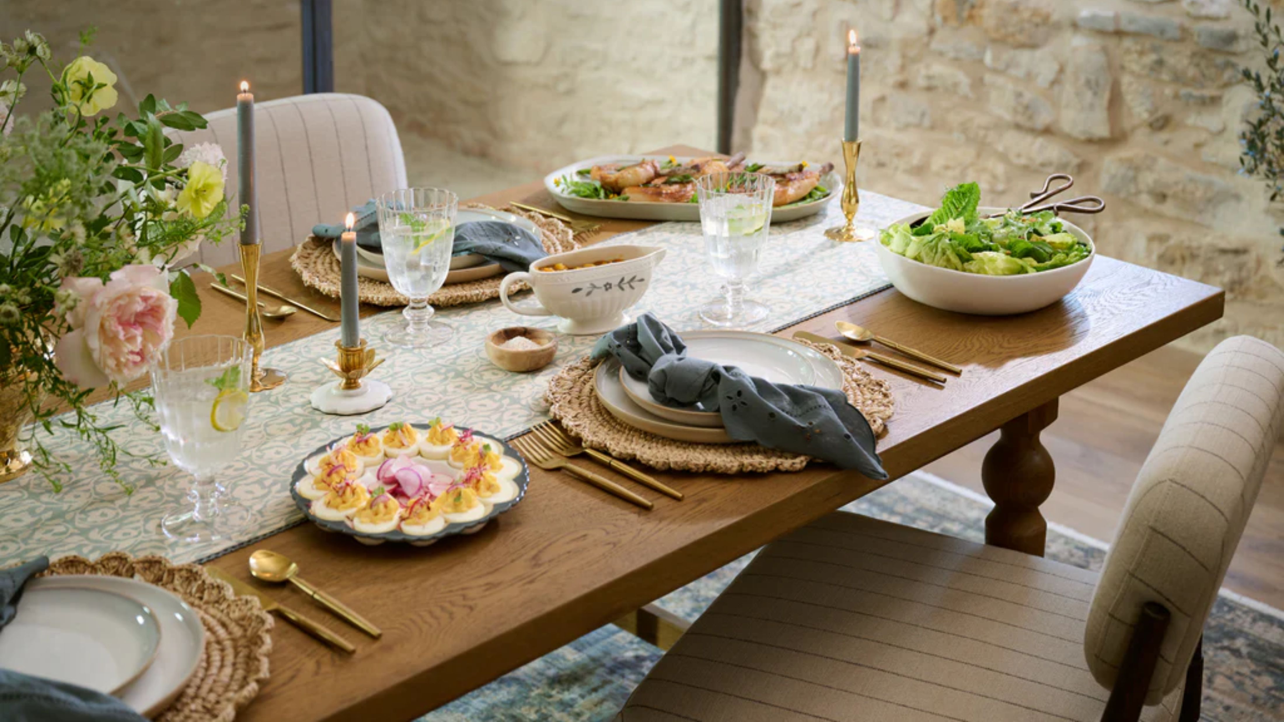Spring tablescape accented with brass tableware, woven chargers, cream dinner plates, and navy blue table linens.