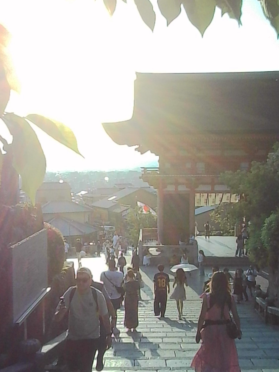 Backlit temple steps in Japan with visitors walking beneath the low sun.