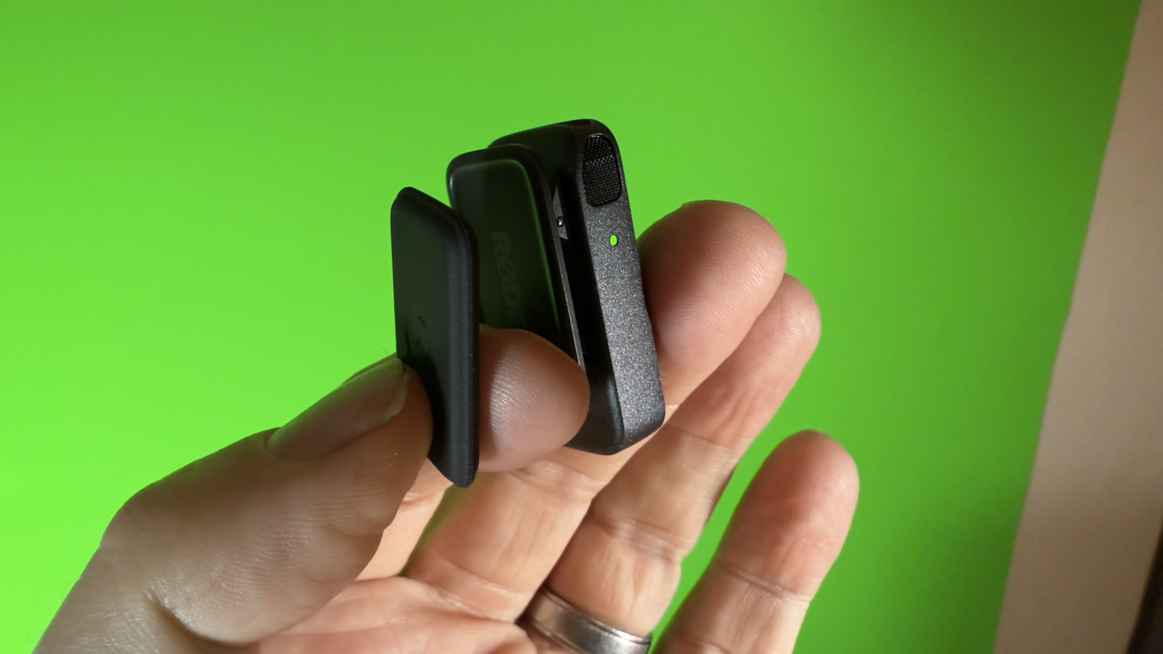 RØDE wireless microphone transmitter held in one hand in front of a green screen