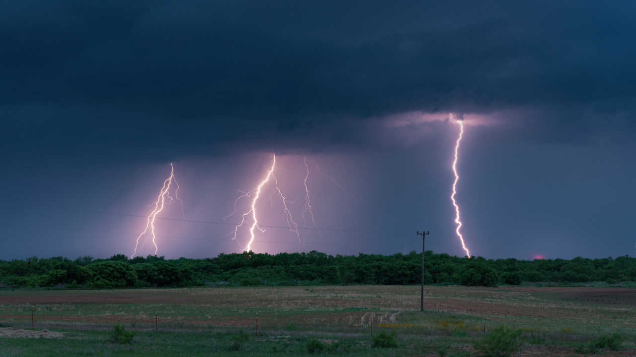 A series of lightning flashes strike the ground from dark gray clouds in the sky.
