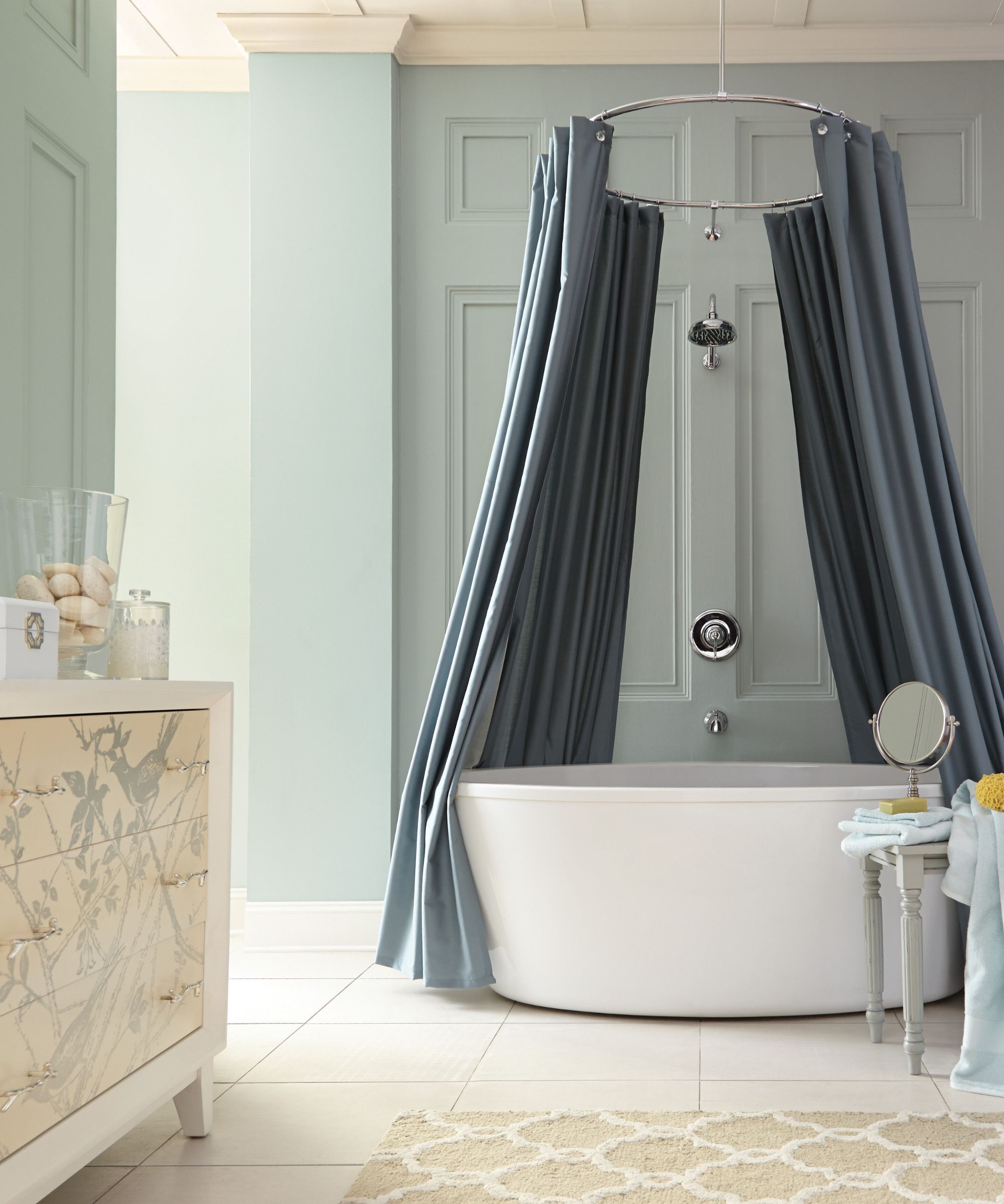 A modern bathroom with walls painted in a mint green, with a blue wrap around shower curtain over the freestanding bath