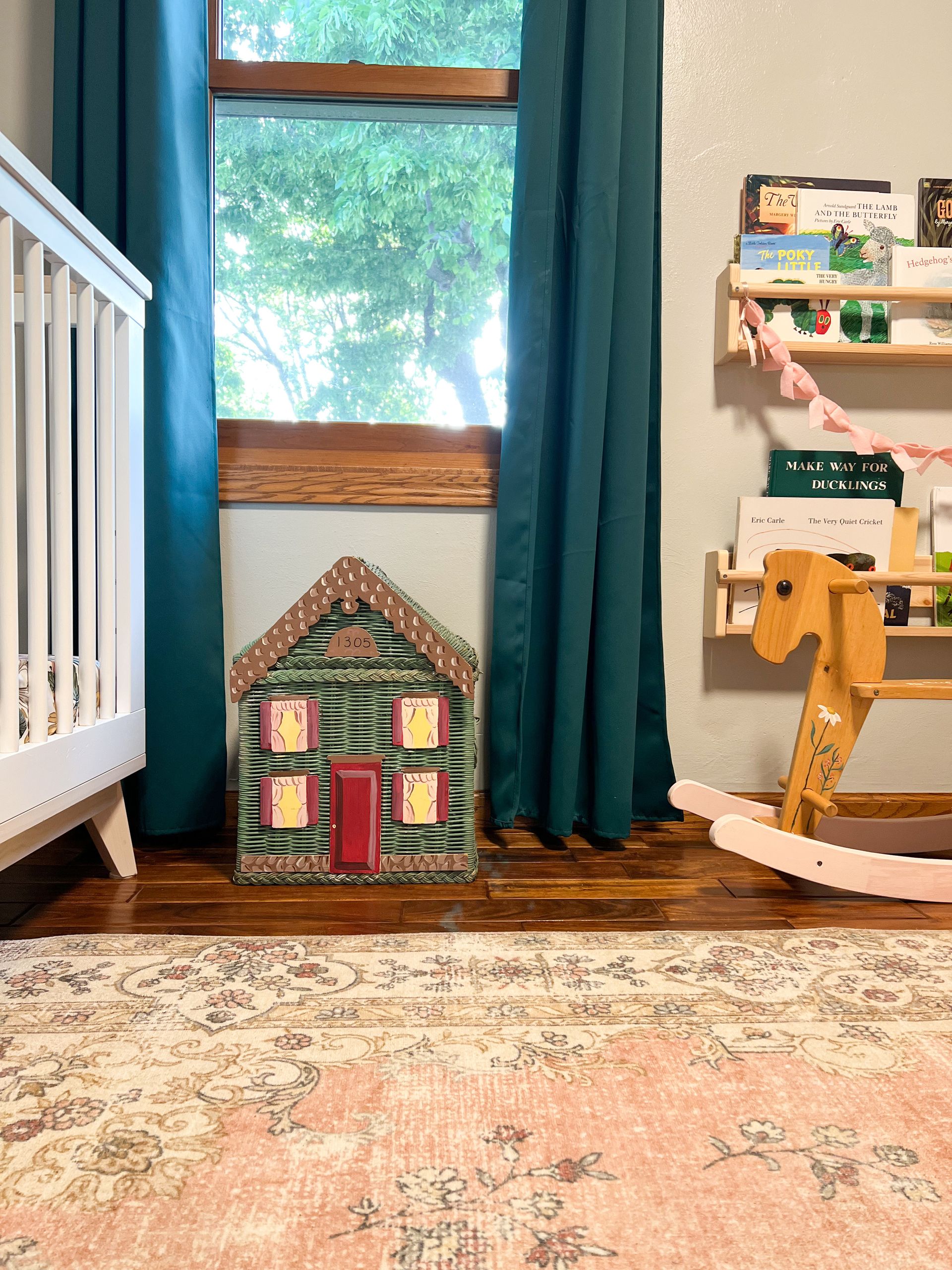 A child's bedroom with a pink rug, blue curtains, and a wicker doll house