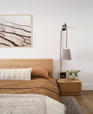 A neutral bedside with natural materials and artwork above the headboard