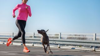 Woman in pink top and black leggings running next to a dog