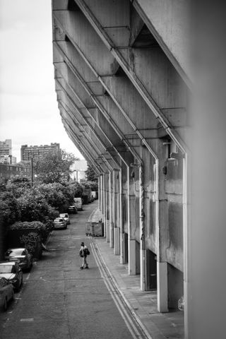 Image of a man crossing a car park behind a tall brutalist building, in black-and-white, taken on the Sigma 18-50mm f/2.8 DC DN | C Canon RF