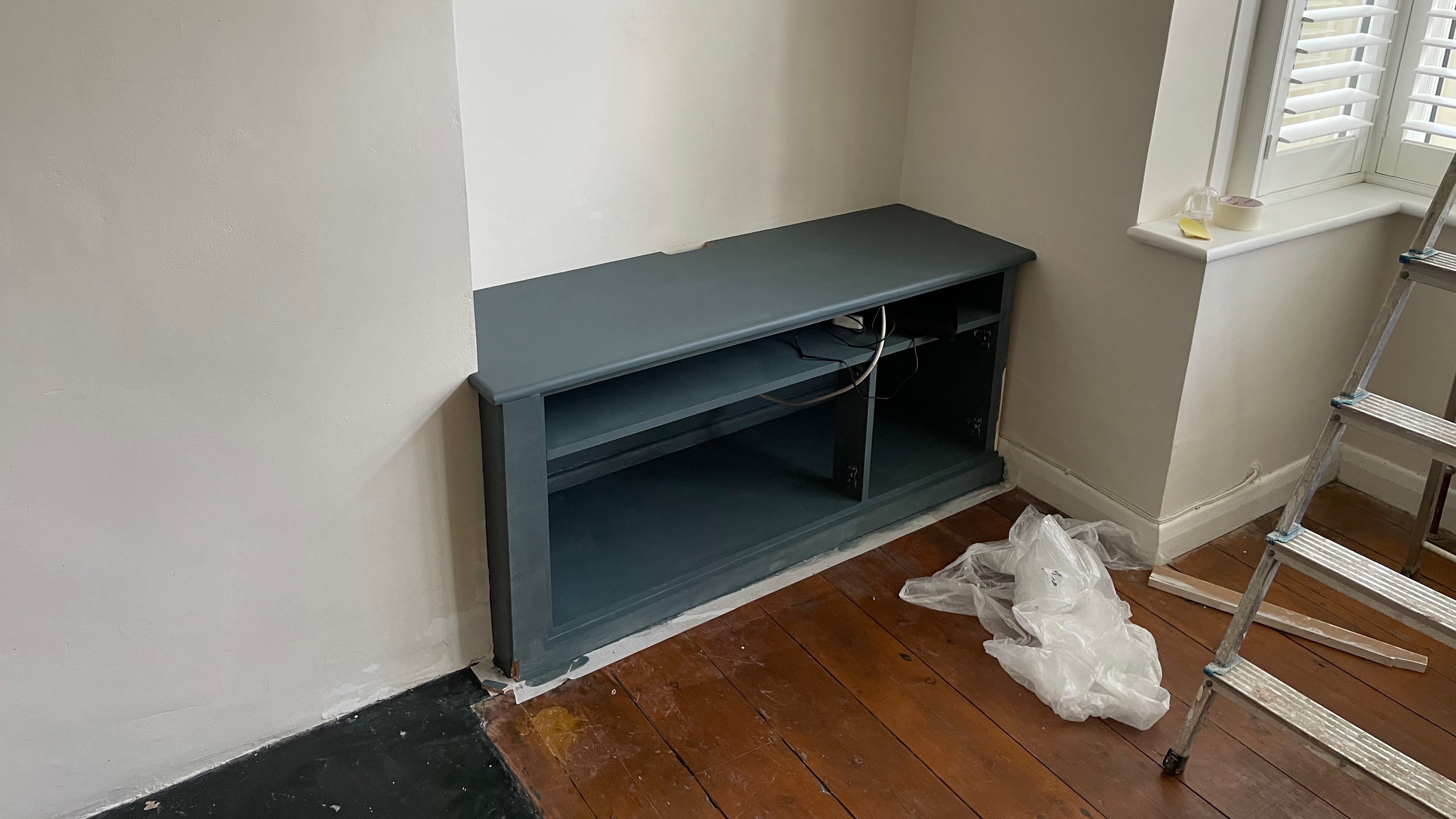 A TV cabinet painted dark blue, but still a work in progress. Next to it is a stepladder.