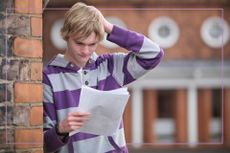 boy looking at exam results paper leaning against red brick wall