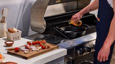 Le Creuset Outdoor BBQ collection shallow casserole on the BBQ with a cutting board with tomatoes and onions on it