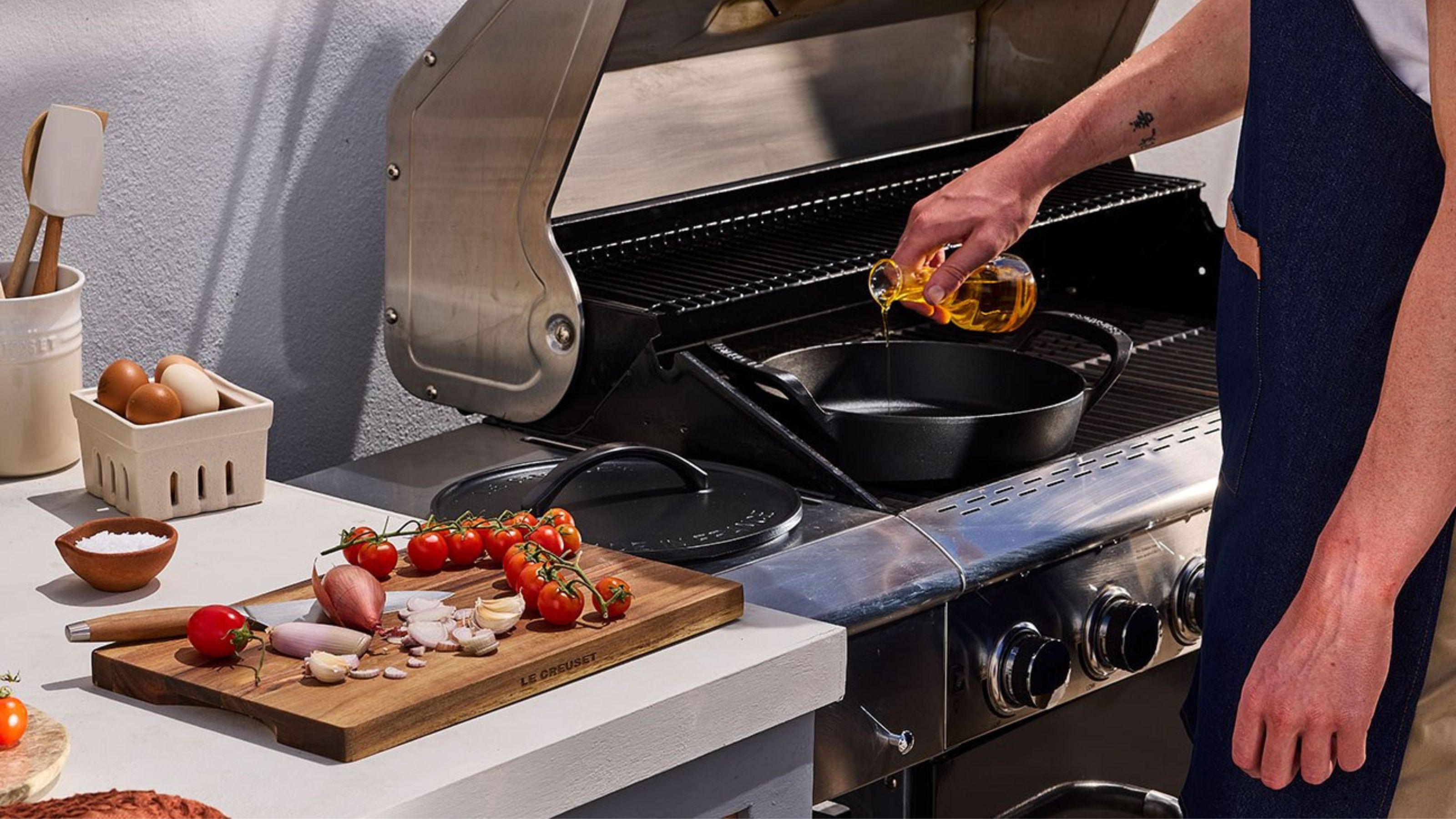 Le Creuset Outdoor BBQ collection shallow casserole on the BBQ with a cutting board with tomatoes and onions on it