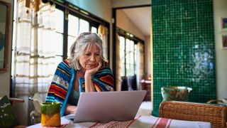 Woman wrapped in blanket sitting at a table looking at a laptop