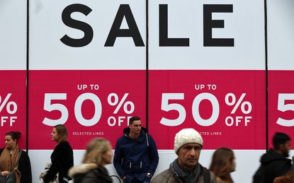 LONDON, ENGLAND - DECEMBER 30: People walk past a sale sign outside a department store on Oxford Street on December 30, 2015 in London, England. Shoppers are continuing to spend as stores off