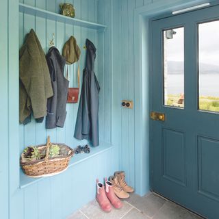 interior of porch with bench, shelf and coat hooks and blue wood panel walls and stone floor