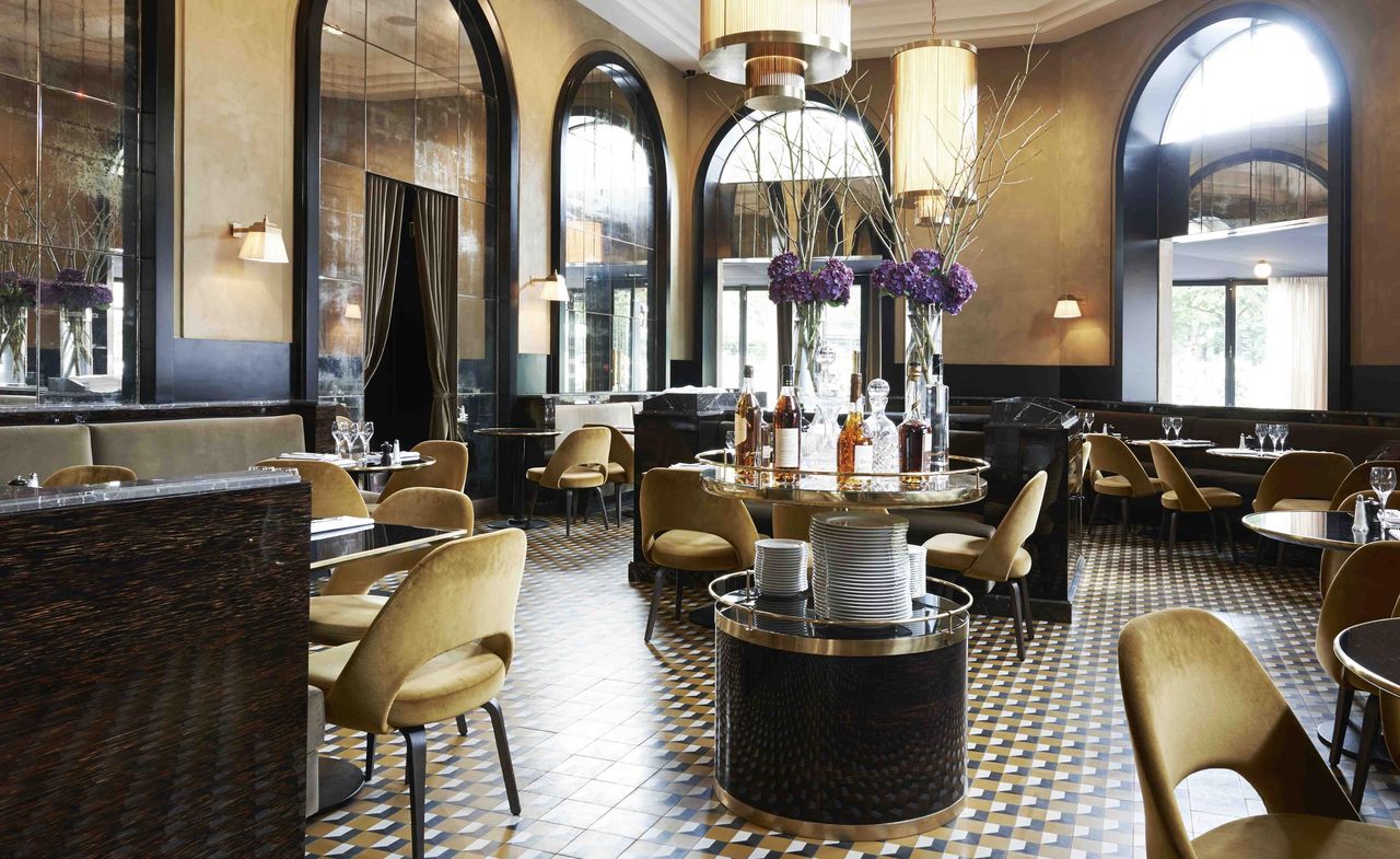 Light brown suede chairs, round tables, centre serving display, checkered black, white and brown tiling