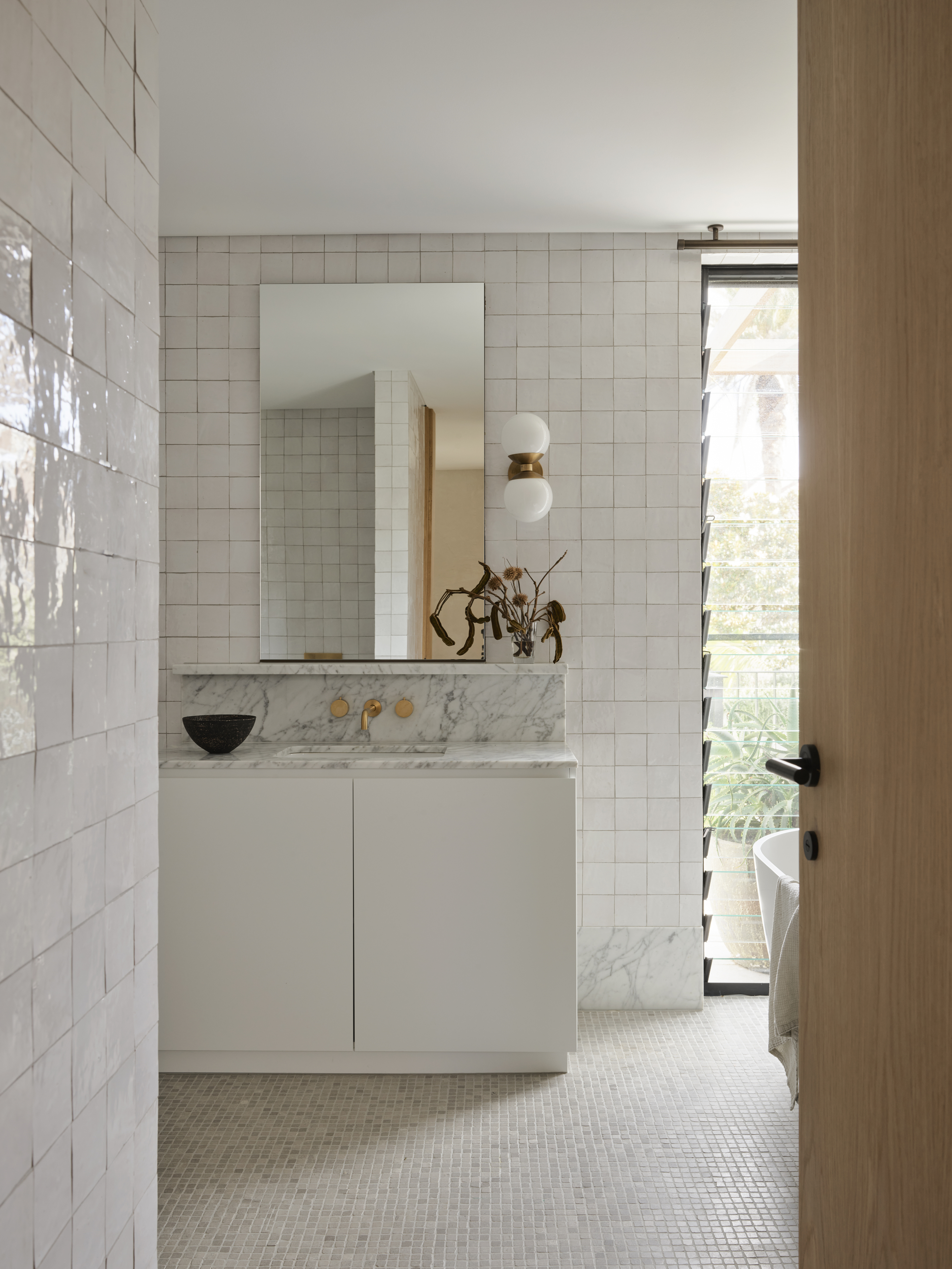 An all-white bathroom with a white and brass sconce next to the mirror