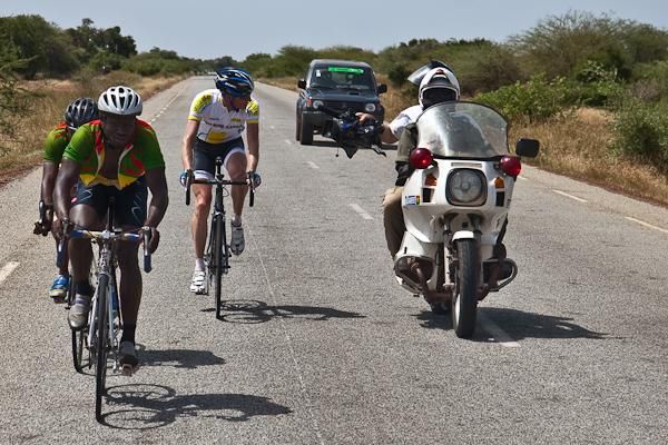 It was a long hard day at the back of the race. Simeon Green of Team Reine Blanche explains his stomach problems to the media while rolling with two Benin riders.
