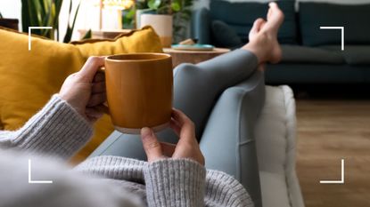 Woman holding cup of tea, lying down on sofa at home, to illustrate the benefits of quitting caffeine