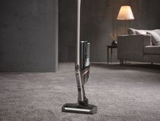 Miele Triflex HX1 Pro standing upright a gray living room with a carpet, gray sofa and a floor lamp