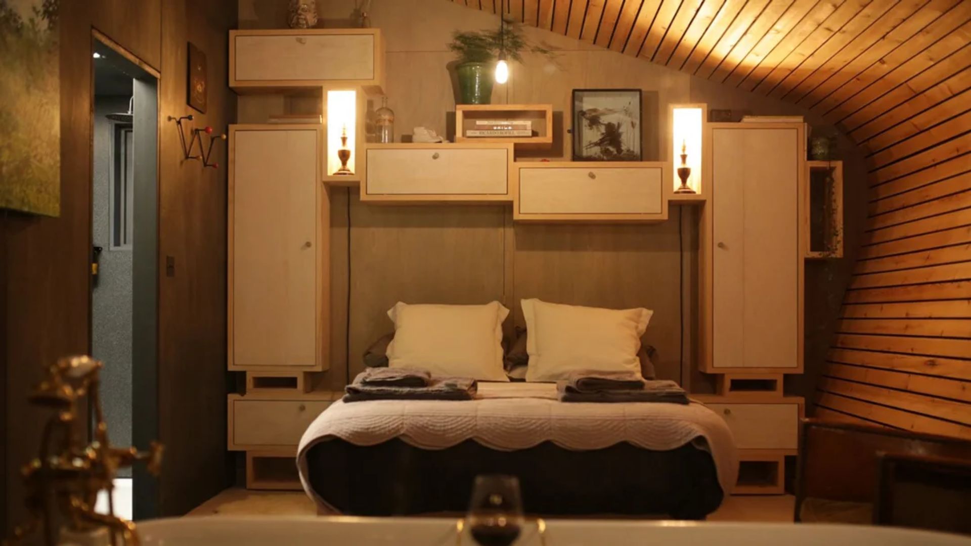 The bedroom of the Hergest Lee Cabin, showing a low bed, wall cabinets, and the lights on