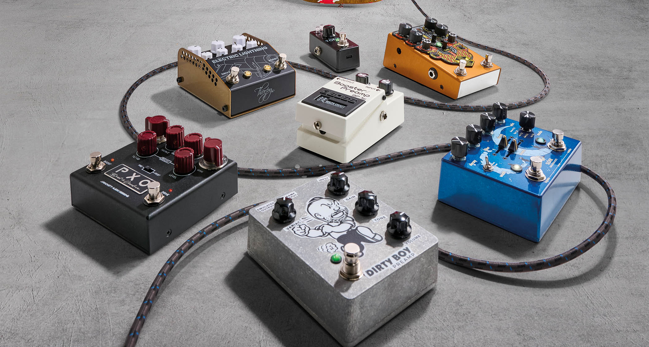 A selection of guitar pedals are photographed against a concrete floor.