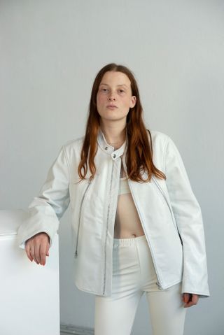 Portrait of woman in white leather jacket and trousers by MM6 and bra top